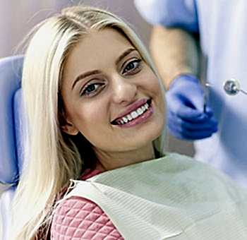 Woman patient smiling in dental chair after a teeth whitening treatment.